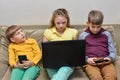 Children play on the phone and laptop. Two boys are sitting with a smartphone, and an older sister with a laptop Royalty Free Stock Photo