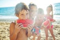 Children play by the sea and eat watermelon.