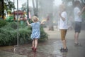 Children play under the water jets in summer park. Breeze on hot day. Playground Royalty Free Stock Photo