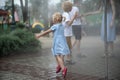 Children play under the water jets in summer park. Breeze on hot day. Walk in the park on sunny day. Playground Royalty Free Stock Photo
