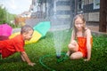 Children playing with garden sprinkler. Brother and sister running and jumping. Summer outdoor water fun in backyard