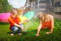 Children playing with garden sprinkler. Brother and sister running and jumping. Summer outdoor water fun in backyard