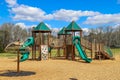 Children playing on a green and brown jungle gym at the park with a green slide surrounded by bare winter trees Royalty Free Stock Photo