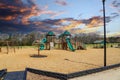 Children playing on a green and brown jungle gym at the park with a green slide surrounded by bare winter trees