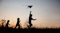 Children playing kite on summer sunset meadow silhouetted Royalty Free Stock Photo