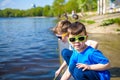 Children playing outdoors in nature: sitting on lake or river shore touching sand in clear water on warm summer or spring day. Royalty Free Stock Photo