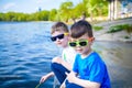 Children playing outdoors in nature: sitting on lake or river shore touching sand in clear water on warm summer or spring day. Royalty Free Stock Photo