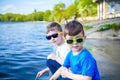 Children playing outdoors in nature: sitting on lake or river shore touching sand in clear water on warm summer or spring day Royalty Free Stock Photo