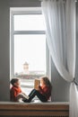 Children reading a books sitting on the window sill at home. Boy and girl reading by the light of sunrise Royalty Free Stock Photo