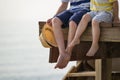 Children relax by the sea sitting on the edge of a wooden jetty with sea background. Sunny joyful summer day