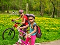 Children ride bicycle on green grass and flowers in park.