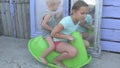 Children ride on green plastic horse rocking on background of mirrors in courtyard of rural house. Beautiful kids