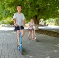 Children ride on scooters on street sidewalk in city outdoor, bright sunny day