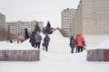 Children ride on a snow slide, parents keep order.