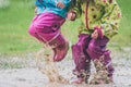 Children in rubber boots and rain clothes jumping in puddle.