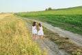 Children run hand in hand in the fresh air among fields and meadows on a narrow sandy path.