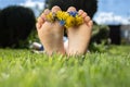 children's bare feet with small wreath of flowers lie on green grass on sunny day. positive atmosphere, hello summer Royalty Free Stock Photo