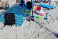 Children`s beach toys, sandals and knapsacks on beach sand near a multi-colored beach blanket Royalty Free Stock Photo