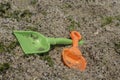 Two spades, shovel, green and orange - children`s beach toys on stony beach with seaweeds. Close up view