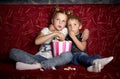 Children`s cinema: A girl and a boy watch a movie at home on a big red sofa in the dark and eat popcorn. Royalty Free Stock Photo