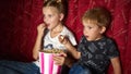 Children`s cinema: A girl and a boy watch a movie at home on a big red sofa in the dark and eat popcorn. Royalty Free Stock Photo