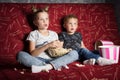 Children`s cinema: A girl and a boy watch a movie at home on a big red sofa in the dark and eat popcorn. Royalty Free Stock Photo