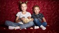 Children`s cinema: A girl and a boy watch a movie at home on a big red sofa in the dark and eat popcorn. Royalty Free Stock Photo