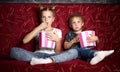 Children`s cinema: A girl and a boy watch a movie at home on a big red sofa in the dark and eat popcorn. Royalty Free Stock Photo