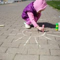 Children`s day. girl draws sun with chalk on sidewalk. kids walk outdoor. summer activity Royalty Free Stock Photo