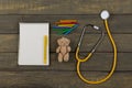 Children& x27;s doctor or pediatrician concept - blank notepad, yellow stethoscope, Teddy bear toy, crayons on wooden background