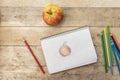 Children`s drawing, apple and colored pencils. Wooden table. Top