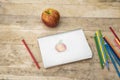 Children`s drawing, apple and colored pencils. Wooden table. Top