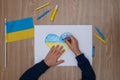 Children`s drawing, flags of ukraine are drawn on a sheet, children`s hands hold a heart made, war between countries, peace