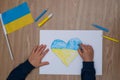 Children`s drawing, flags of ukraine are drawn on a sheet, children`s hands hold a heart made, war between countries, peace