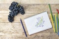 Children`s drawing, grapes and colored pencils. Wooden table. To