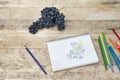 Children`s drawing, grapes and colored pencils. Wooden table. To