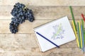 Children`s drawing, grapes and colored pencils. Wooden table. To
