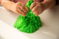 Children`s games. Sand. Child development. Close up of children`s hands playing with green kinetic sand on white table; selectiv Royalty Free Stock Photo