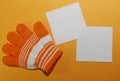 Children`s glove, on the child`s hand, orange striped lies on a yellow surface with two white square shaped blank sheets for writi Royalty Free Stock Photo