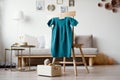 Children`s green knitted dress hangs on hanger on chair in room. A dress made of woolen thread is tied with hands on knitting Royalty Free Stock Photo