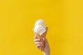 Children`s hand holds delicious vanilla ice cream cone on a bright yellow background Royalty Free Stock Photo