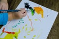 children's hand paints with brush, little girl preschooler 3 years creates bright picture on paper, childish naive