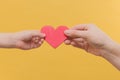 Children`s hand and the hand of a woman hold a red heart by the edges on a yellow background. The idea is peace, mutual