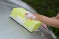 Children`s hand with a yellow sponge with foam washes the car