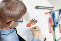 Children`s hands hold a green felt-tip pen and draw a green guy on a white piece of paper.