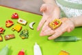 Children`s hands are holding a decorated rectangular cake. Colorful cinnamon cakes lie on the green table in the background. Tubes