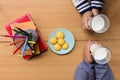 Children`s hands holding milk glasses and snack with notebook and color pencil on wooden table.Top view Royalty Free Stock Photo