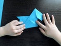 Children's hands make origami dog from blue paper. Children's creativity concept. Development of fine motor skills