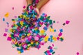 Children`s hands scatter colorful confetti. Top view, horizontally on a pink background, with space Royalty Free Stock Photo