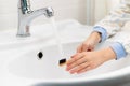 Children`s hands wash a bamboo toothbrush under running water over a white washbasin in the bathroom. Personal hygiene Royalty Free Stock Photo